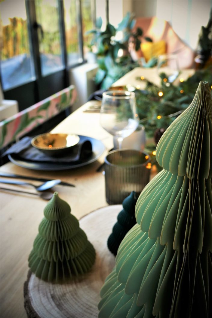 Table de Noël ambiance sous bois réalisée par Studio Candy pour For Me Lab - assiettes noir mat, bols dorés brillant, serviettes en lin, branches de sapin, boules de Noël en papier, pommes de pin