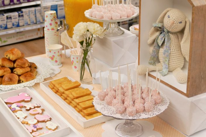 Sweet table thème bébé pour le magasin Toys'R Us de la Défense. Scénographie par Studio Candy. Cake pops roses, financiers, jus d'orange, viennoiseries, sablés décorés poussette, chausson, bavoir, body... et décoration thème Baby Shower