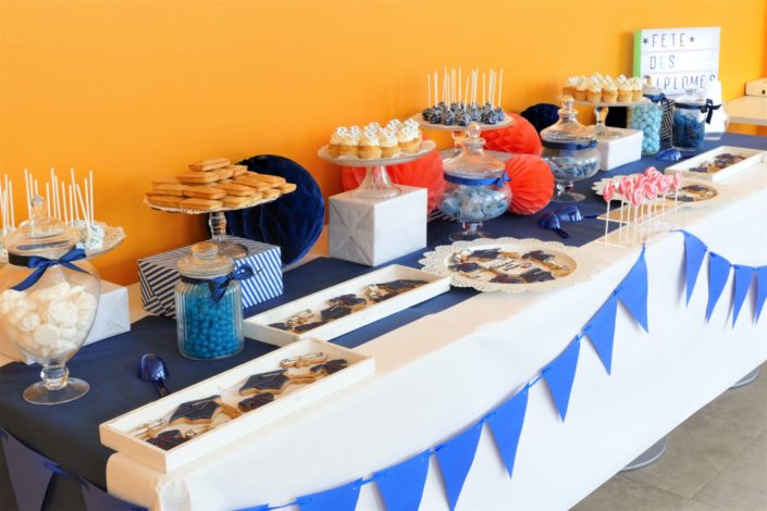 Fête des diplômés chez Babilou par Studio Candy - Sweet table, candy bar bleu, blanc et corail - Sablés décorés diplômes, toge, bonbons, sucettes, cupcakes avec logo, décoration