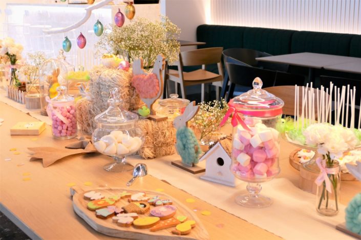 Goûter de Pâques naturel et pastel avec bottes de foin, oeufs en chocolat, bonbons, cake pops, fleurs, lapins et poules, nids meringue, sablés décorés