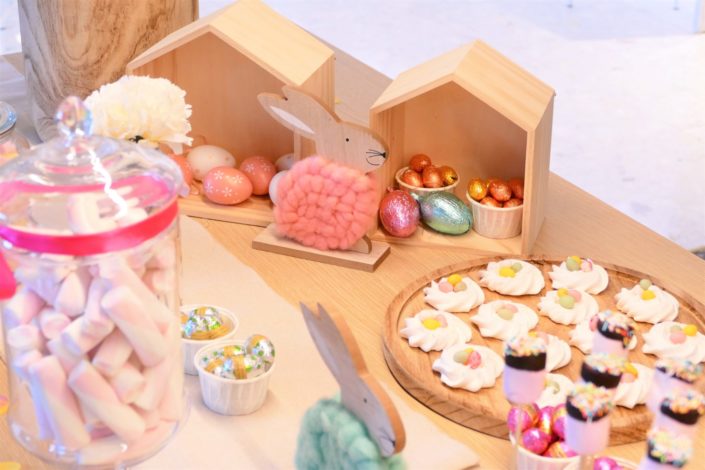 Goûter de Pâques naturel et pastel avec bottes de foin, oeufs en chocolat, bonbons, cake pops, fleurs, lapins et poules, nids meringue, sablés décorés