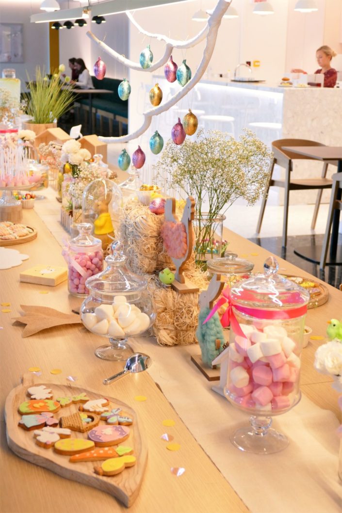 Goûter de Pâques naturel et pastel avec bottes de foin, oeufs en chocolat, bonbons, cake pops, fleurs, lapins et poules, nids meringue, sablés décorés