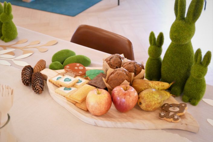 Petit déjeuner nature pour le lancement de la gamme de jouets Clementoni - brownie au noix, fruits frais, sablés décorés, muffins myrtille - décoration eucalyptus, lapins en mousse, pommes de pin, lin froissé beige