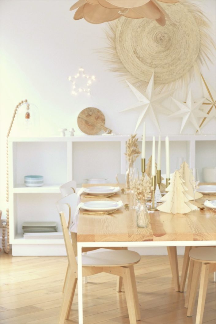 Table de Noël ambiance Laponie avec assiettes en céramique blanche, serviettes en lin blanc, flocons de neige, sapins en bois, bougeoirs dorés, fleurs séchées, couverts dorés mat