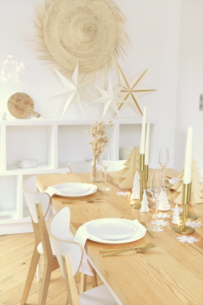 Table de Noël ambiance Laponie avec assiettes en céramique blanche, serviettes en lin blanc, flocons de neige, sapins en bois, bougeoirs dorés, fleurs séchées, couverts dorés mat