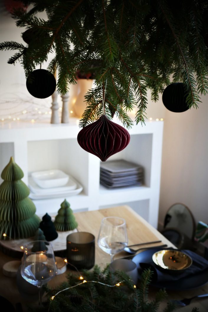 Table de Noël ambiance sous bois réalisée par Studio Candy pour For Me Lab - assiettes noir mat, bols dorés brillant, serviettes en lin, branches de sapin, boules de Noël en papier, pommes de pin