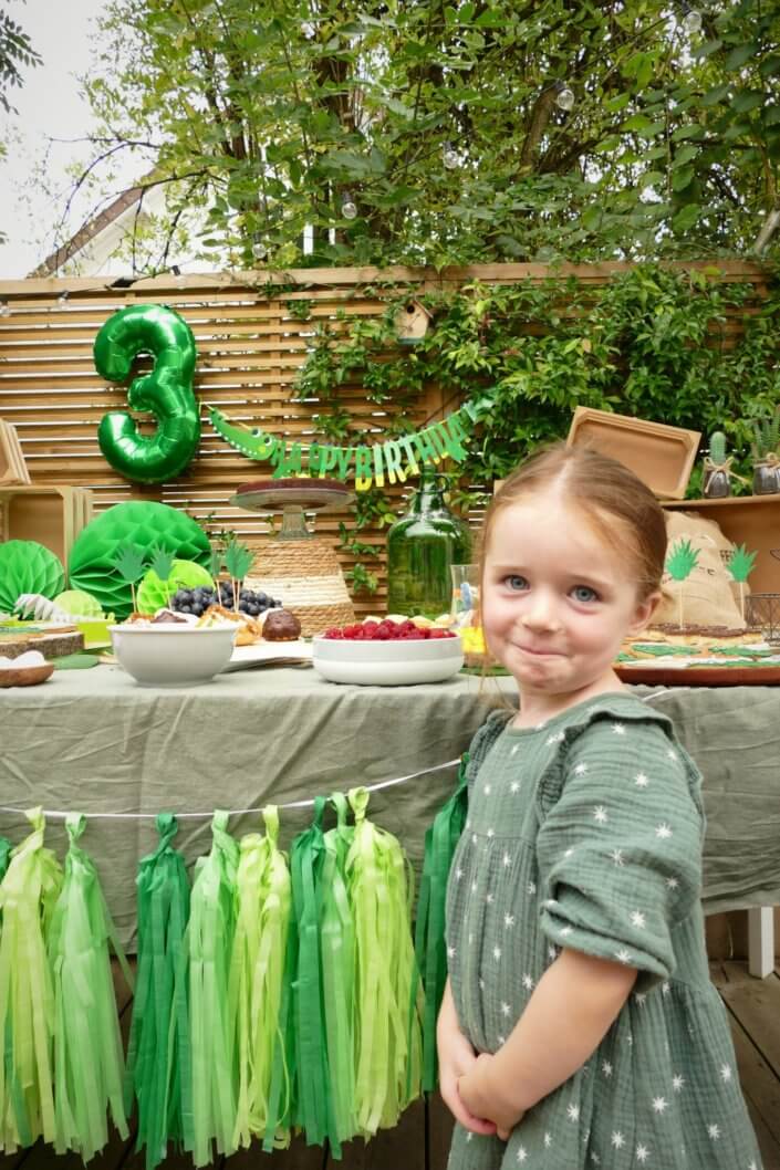 Anniversaire crocodile jungle avec sablés décorés , petits choux farcis, raisins, financiers amande, gâteaux au chocolat, bonbons. Décoration verte, feuilles tropicales monstera, boîtes crocodiles, vases, guirlande et ballons hélium.