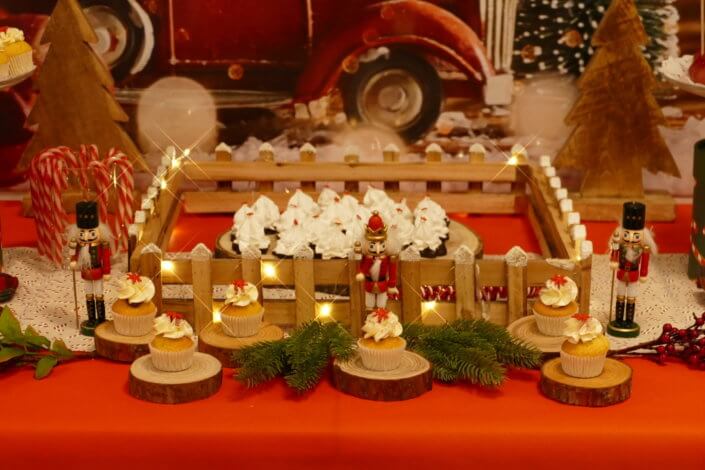 Goûter de Noël traditionnel avec petits sablés, cakepops rouges pailletés, chamallows bonhommes de neige, sapins meringue, petits oursons guimauve. Décoration en rouge, or, vert sapin avec des sucres d'orges, des bonbons, des sapins en bois