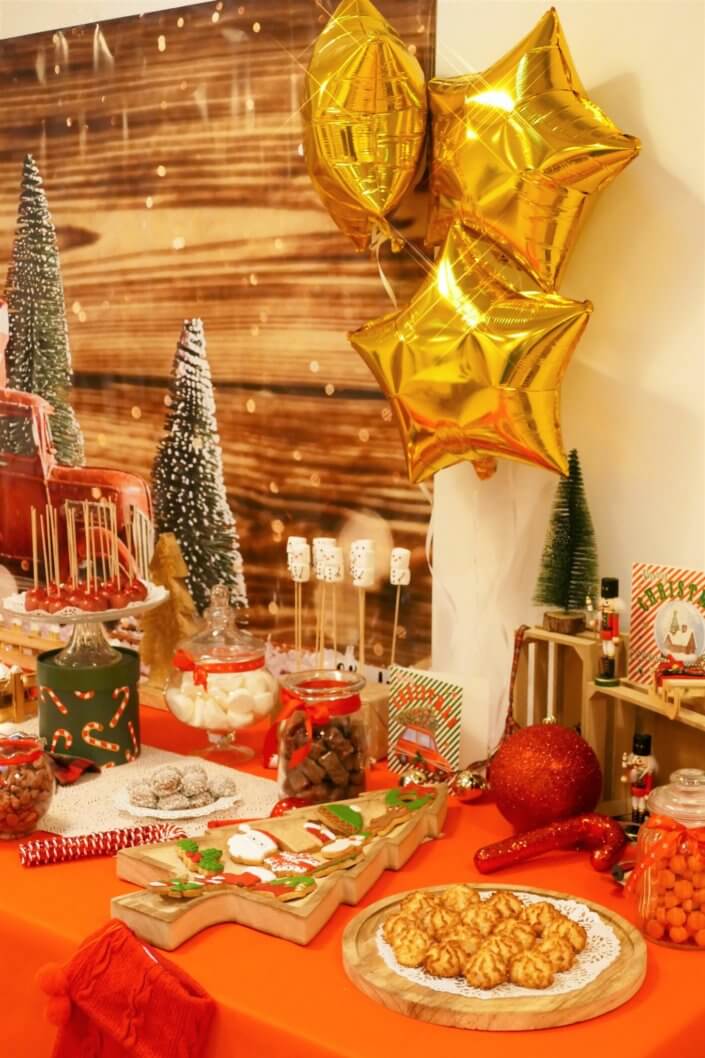 Goûter de Noël traditionnel avec petits sablés, cakepops rouges pailletés, chamallows bonhommes de neige, sapins meringue, petits oursons guimauve. Décoration en rouge, or, vert sapin avec des sucres d'orges, des bonbons, des sapins en bois