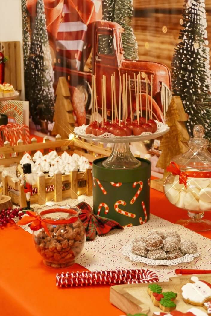 Goûter de Noël traditionnel avec petits sablés, cakepops rouges pailletés, chamallows bonhommes de neige, sapins meringue, petits oursons guimauve. Décoration en rouge, or, vert sapin avec des sucres d'orges, des bonbons, des sapins en bois