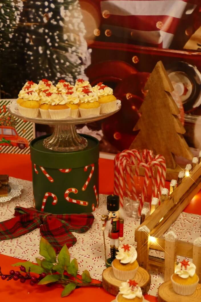 Goûter de Noël traditionnel avec petits sablés, cakepops rouges pailletés, chamallows bonhommes de neige, sapins meringue, petits oursons guimauve. Décoration en rouge, or, vert sapin avec des sucres d'orges, des bonbons, des sapins en bois