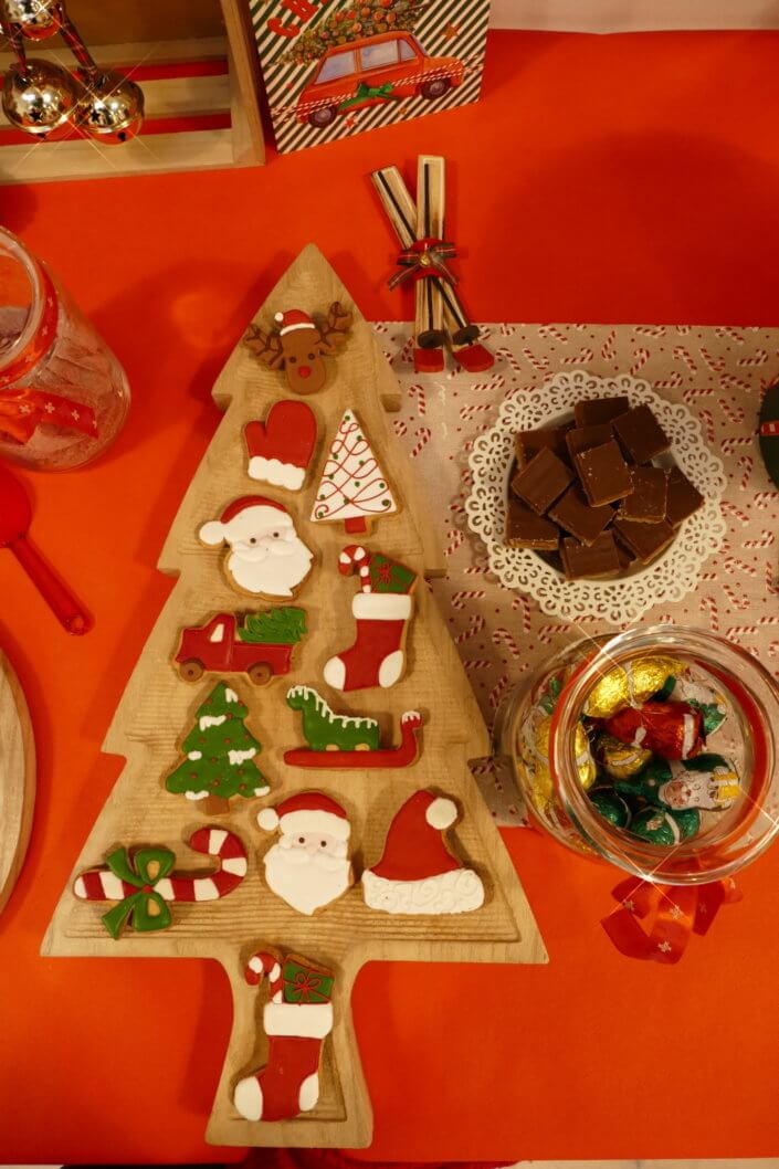 Goûter de Noël traditionnel avec petits sablés, cakepops rouges pailletés, chamallows bonhommes de neige, sapins meringue, petits oursons guimauve. Décoration en rouge, or, vert sapin avec des sucres d'orges, des bonbons, des sapins en bois