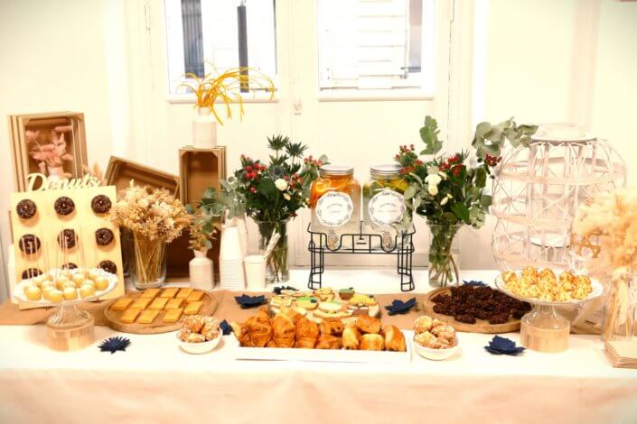 Réalisation d'une table gourmande décorée avec cake pops, sablés décorés, roses des sables, financiers, fleurs fraîches, fontaines à boissons d'eaux infusées, chemin de table en toile de jute, lanternes en bois.