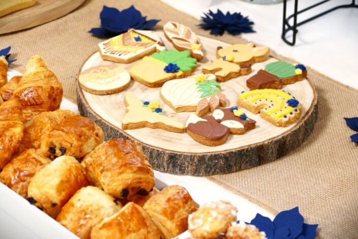 Réalisation d'une table gourmande décorée avec cake pops, sablés décorés, roses des sables, financiers, fleurs fraîches, fontaines à boissons d'eaux infusées, chemin de table en toile de jute, lanternes en bois.