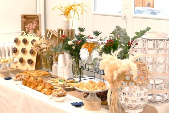 Réalisation d'une table gourmande décorée avec cake pops, sablés décorés, roses des sables, financiers, fleurs fraîches, fontaines à boissons d'eaux infusées, chemin de table en toile de jute, lanternes en bois.