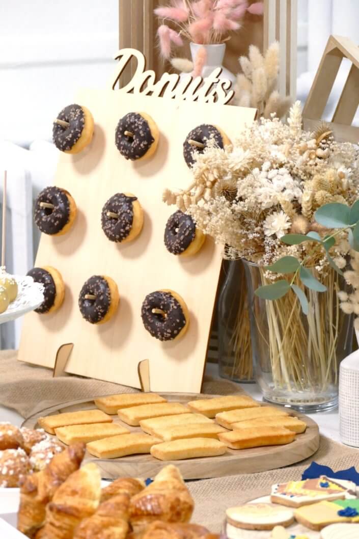 Réalisation d'une table gourmande décorée avec cake pops, sablés décorés, roses des sables, financiers, fleurs fraîches, fontaines à boissons d'eaux infusées, chemin de table en toile de jute, lanternes en bois.