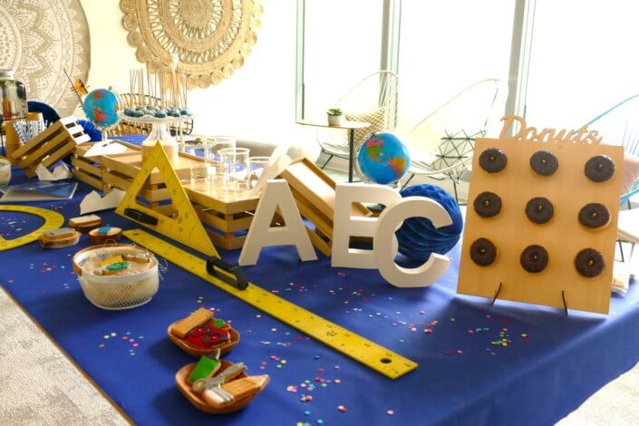 Goûter thème Back to school pour les stagiaires avec grandes règles jaunes, globe terrestre, sablés décorés cahier d'école, donuts au chocolat et cakepops bleu marine