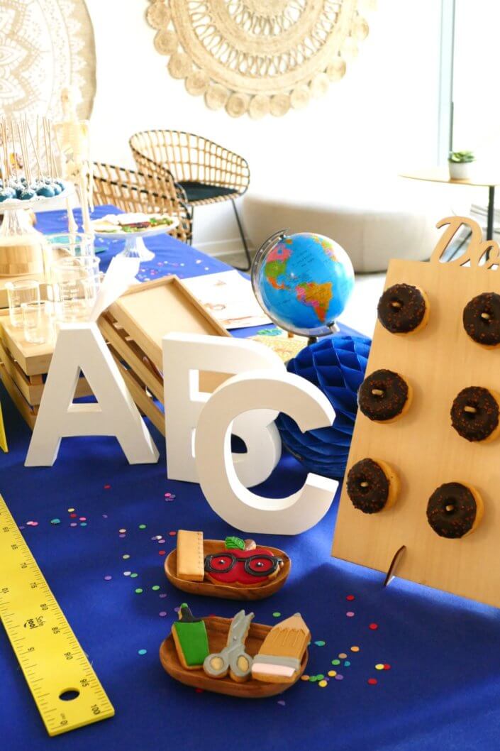 Goûter thème Back to school pour les stagiaires avec grandes règles jaunes, globe terrestre, sablés décorés cahier d'école, donuts au chocolat et cakepops bleu marine