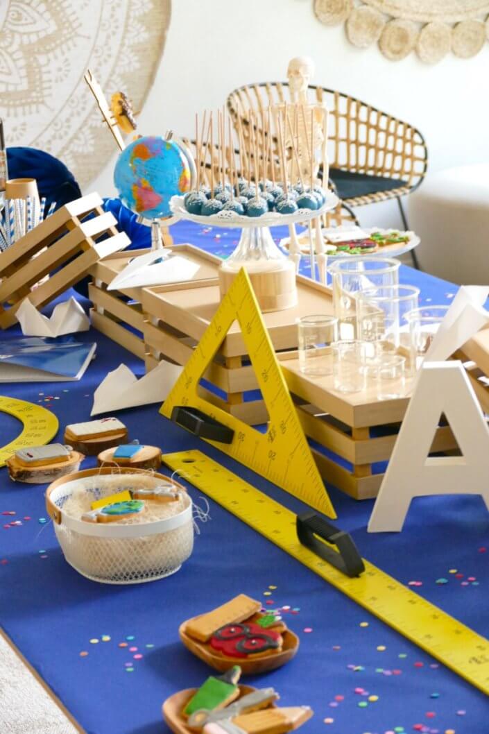 Goûter thème Back to school pour les stagiaires avec grandes règles jaunes, globe terrestre, sablés décorés cahier d'école, donuts au chocolat et cakepops bleu marine