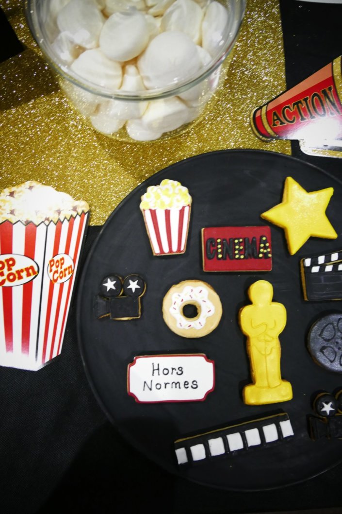 Goûter thème cinéma pour le film Hors Normes avec sablés décorés pot de pop corn, ticket de cinéma, caméra, clap, étoile dorée, bobine, candy bar et décoration sur mesure