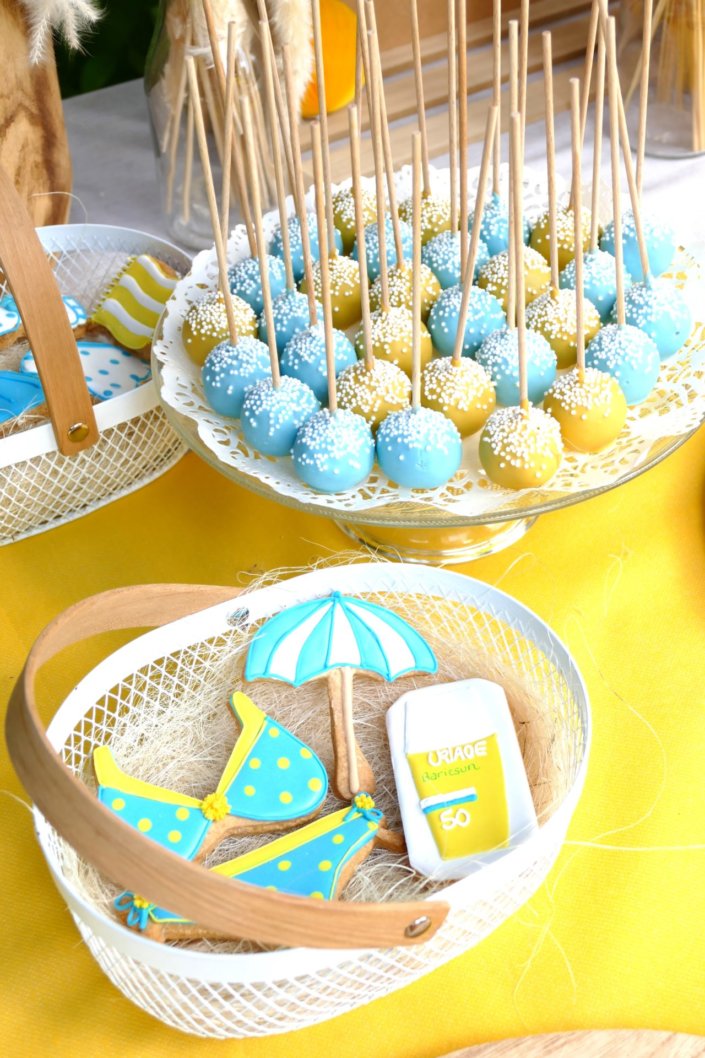 Pool party Uriage avec buffet décoré sur mesure de fleurs séchées, lanternes en bois, patisseries et sablés décorés en forme de crème solaire, cakepops, financiers, gâteaux