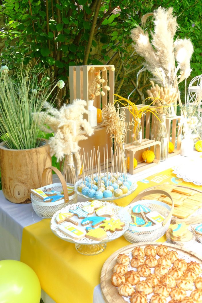 Pool party Uriage avec buffet décoré sur mesure de fleurs séchées, lanternes en bois, patisseries et sablés décorés en forme de crème solaire, cakepops, financiers, gâteaux