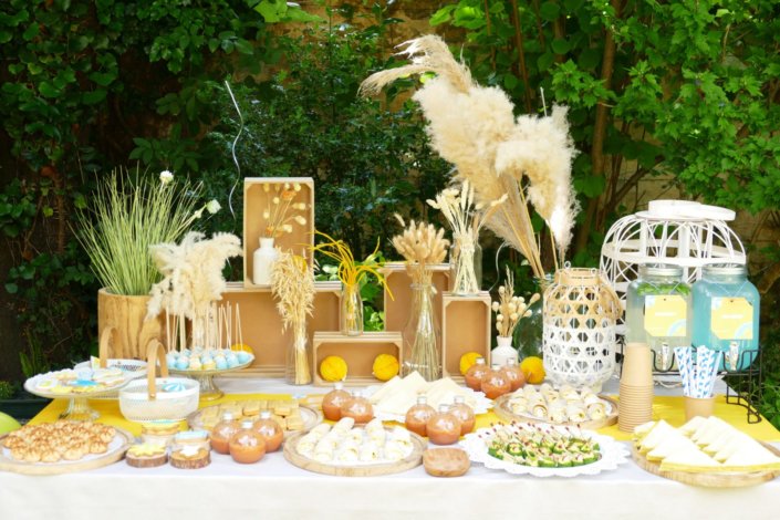 Pool party Uriage avec buffet décoré sur mesure de fleurs séchées, lanternes en bois, patisseries et sablés décorés en forme de crème solaire, cakepops, financiers, gâteaux