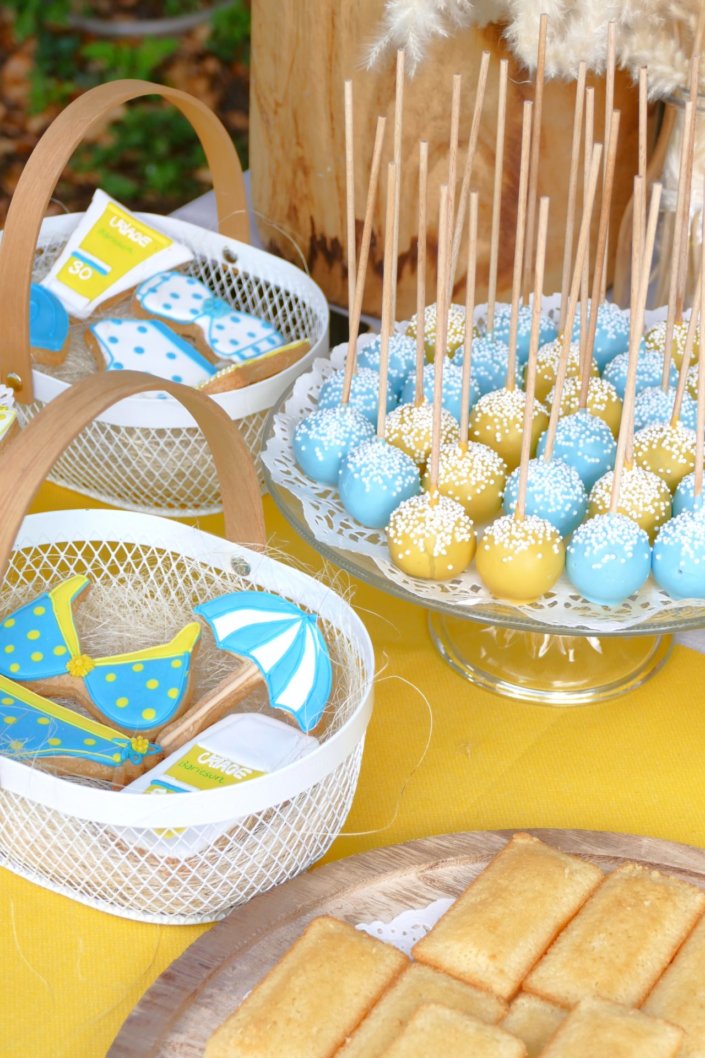 Pool party Uriage avec buffet décoré sur mesure de fleurs séchées, lanternes en bois, patisseries et sablés décorés en forme de crème solaire, cakepops, financiers, gâteaux