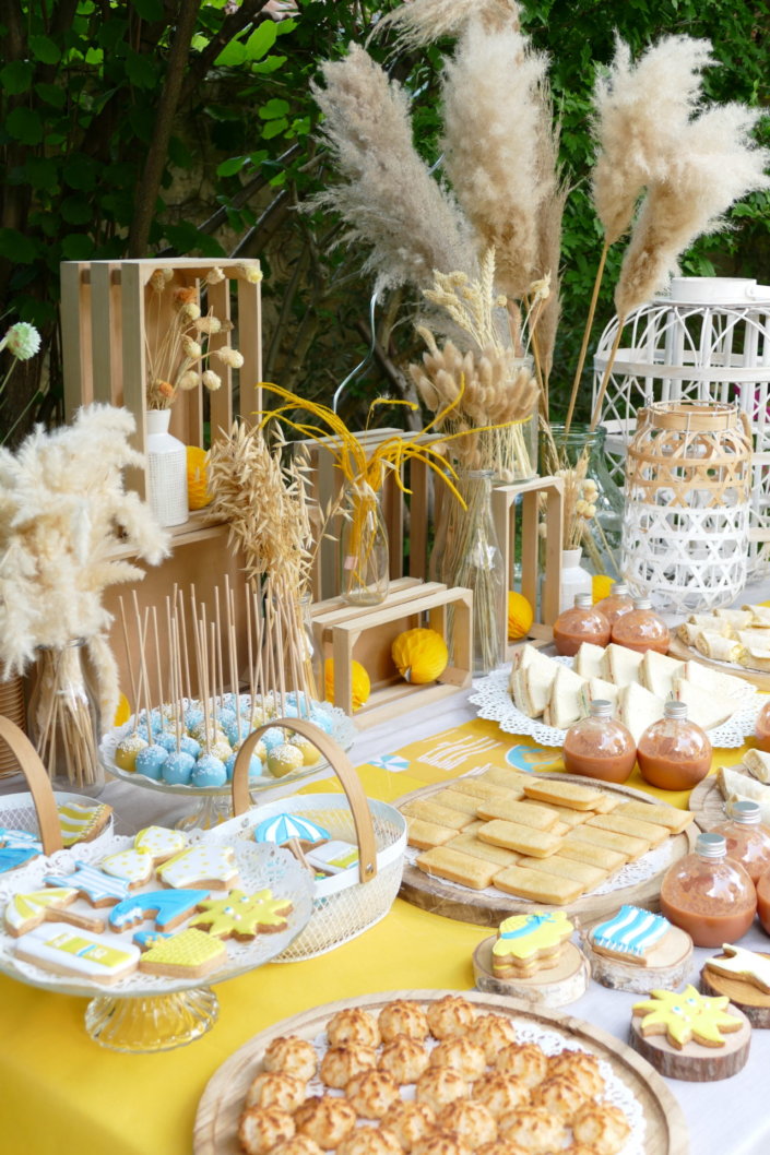 Pool party Uriage avec buffet décoré sur mesure de fleurs séchées, lanternes en bois, patisseries et sablés décorés en forme de crème solaire, cakepops, financiers, gâteaux
