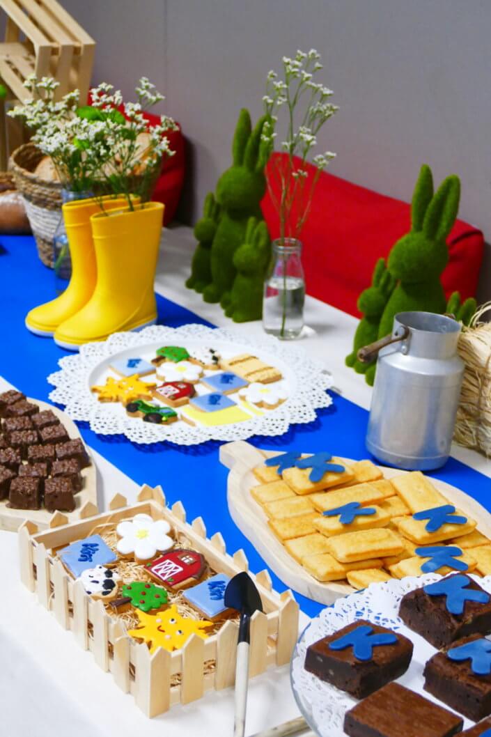 Table décorée pour Kiri avec petits sablés sur mesure : ferme, botte de foin, tracteur, vache, financiers, mini cannelés, brownie chocolat et bar à pain pour se tartiner son kiri ! Décoration champêtre enfantine avec de petites bottes fleuries, des fleurs des champs, des bottes de foin.