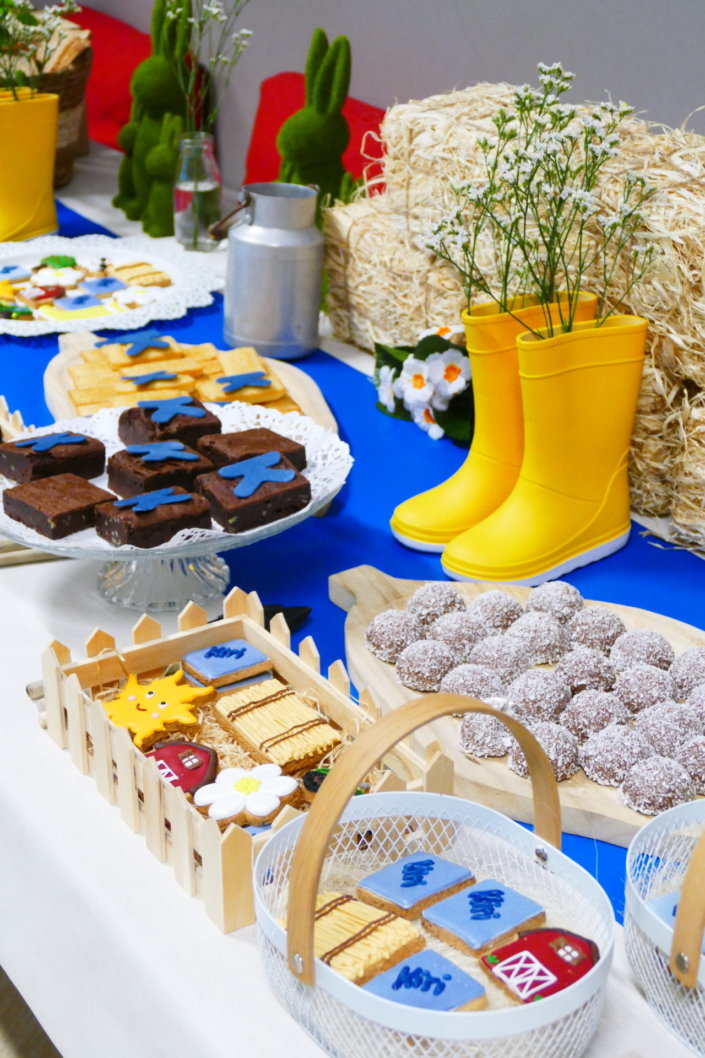 Table décorée pour Kiri avec petits sablés sur mesure : ferme, botte de foin, tracteur, vache, financiers, mini cannelés, brownie chocolat et bar à pain pour se tartiner son kiri ! Décoration champêtre enfantine avec de petites bottes fleuries, des fleurs des champs, des bottes de foin.