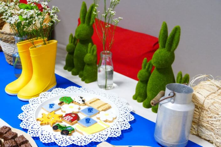 Table décorée pour Kiri avec petits sablés sur mesure : ferme, botte de foin, tracteur, vache, financiers, mini cannelés, brownie chocolat et bar à pain pour se tartiner son kiri ! Décoration champêtre enfantine avec de petites bottes fleuries, des fleurs des champs, des bottes de foin.