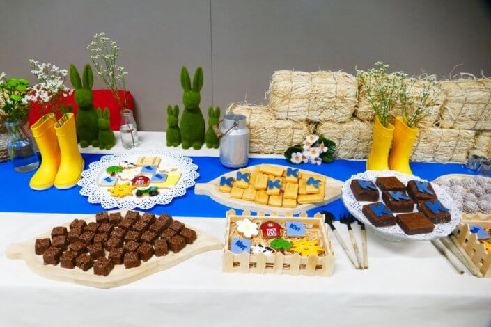 Table décorée pour Kiri avec petits sablés sur mesure : ferme, botte de foin, tracteur, vache, financiers, mini cannelés, brownie chocolat et bar à pain pour se tartiner son kiri ! Décoration champêtre enfantine avec de petites bottes fleuries, des fleurs des champs, des bottes de foin.