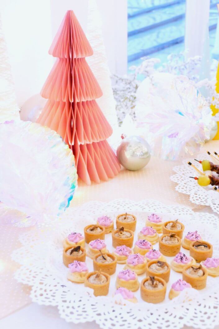 Table de Noël pour la soirée influence des parfums Adopt' - Décoration en blanc et rose, sablés décorés de Noël sur mesure, financiers, brownie, fontaines à boissons et pièces salées roses sur mesure.