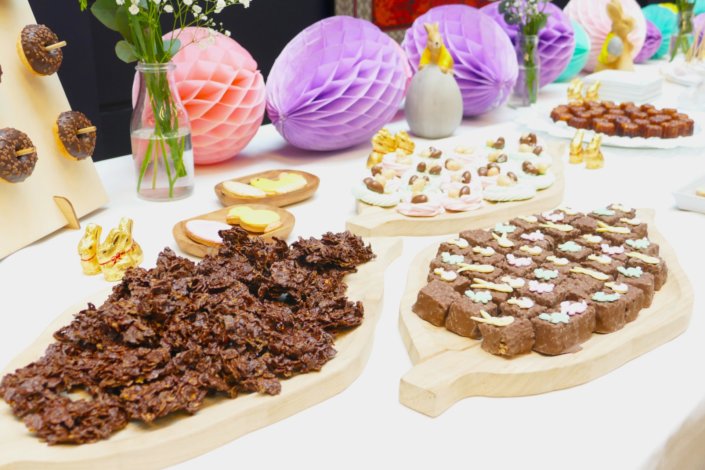 Goûter de Pâques avec oeufs en chocolat, carrot cake, cake marbré vanille chocolat, cakepops, fruits, financiers, roses des sables, sablés décorés, décoration bottes de foin et fleurs fraîches par STUDIO CANDY