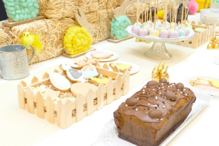 Goûter de Pâques avec oeufs en chocolat, carrot cake, cake marbré vanille chocolat, cakepops, fruits, financiers, roses des sables, sablés décorés, décoration bottes de foin et fleurs fraîches par STUDIO CANDY