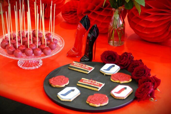 Lancement du parfum Very Good Girl de Carolina Herrera avec Studio Candy : table sur mesure avec des sablés décorés, cakepops rouges pailletés, madeleines, brownie, nappage rouge, bouquets de roses rouges