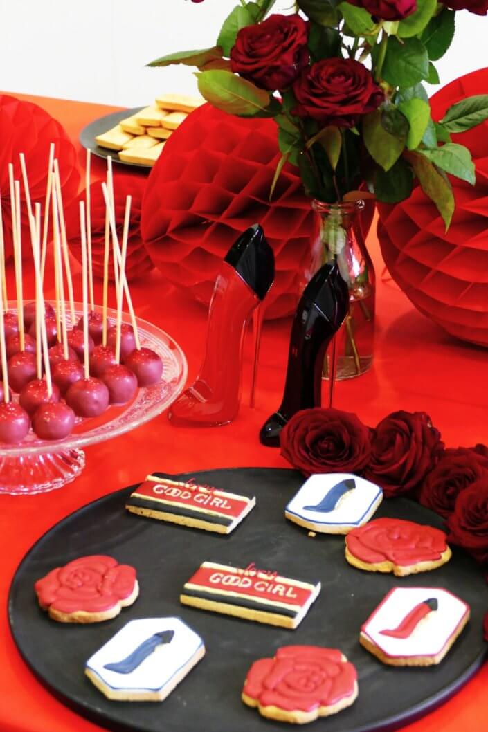 Lancement du parfum Very Good Girl de Carolina Herrera avec Studio Candy : table sur mesure avec des sablés décorés, cakepops rouges pailletés, madeleines, brownie, nappage rouge, bouquets de roses rouges