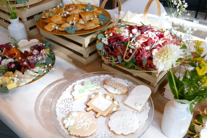 Jolie table thème mariage avec petites brochettes, salades, planche de fromages, feuilletés, sablés décorés wedding day, financiers, décoration or, blanc et petits bouquets de gypsophille