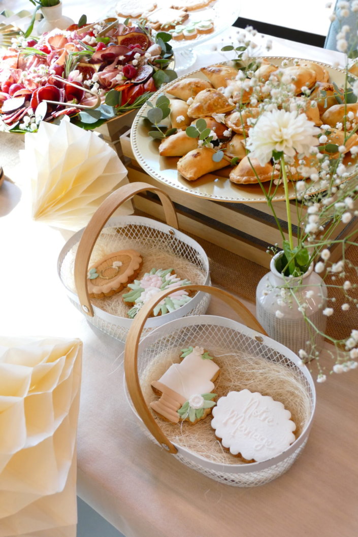 Jolie table thème mariage avec petites brochettes, salades, planche de fromages, feuilletés, sablés décorés wedding day, financiers, décoration or, blanc et petits bouquets de gypsophille