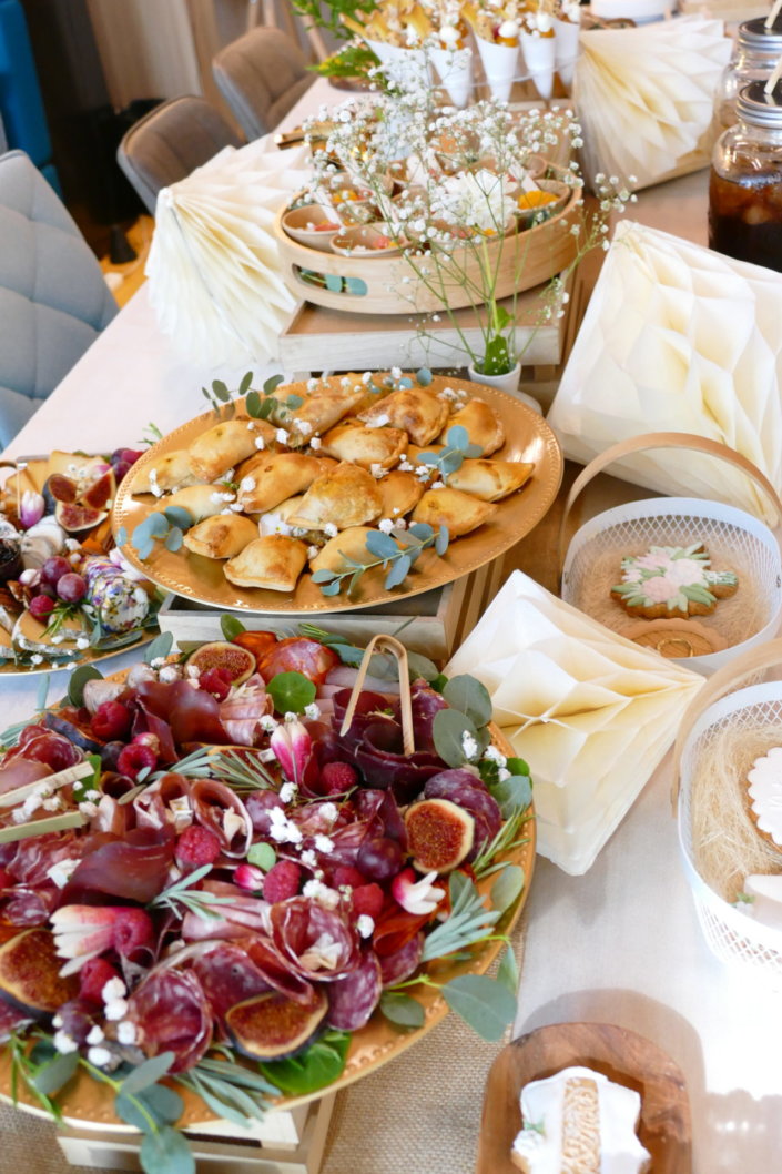 Jolie table thème mariage avec petites brochettes, salades, planche de fromages, feuilletés, sablés décorés wedding day, financiers, décoration or, blanc et petits bouquets de gypsophille