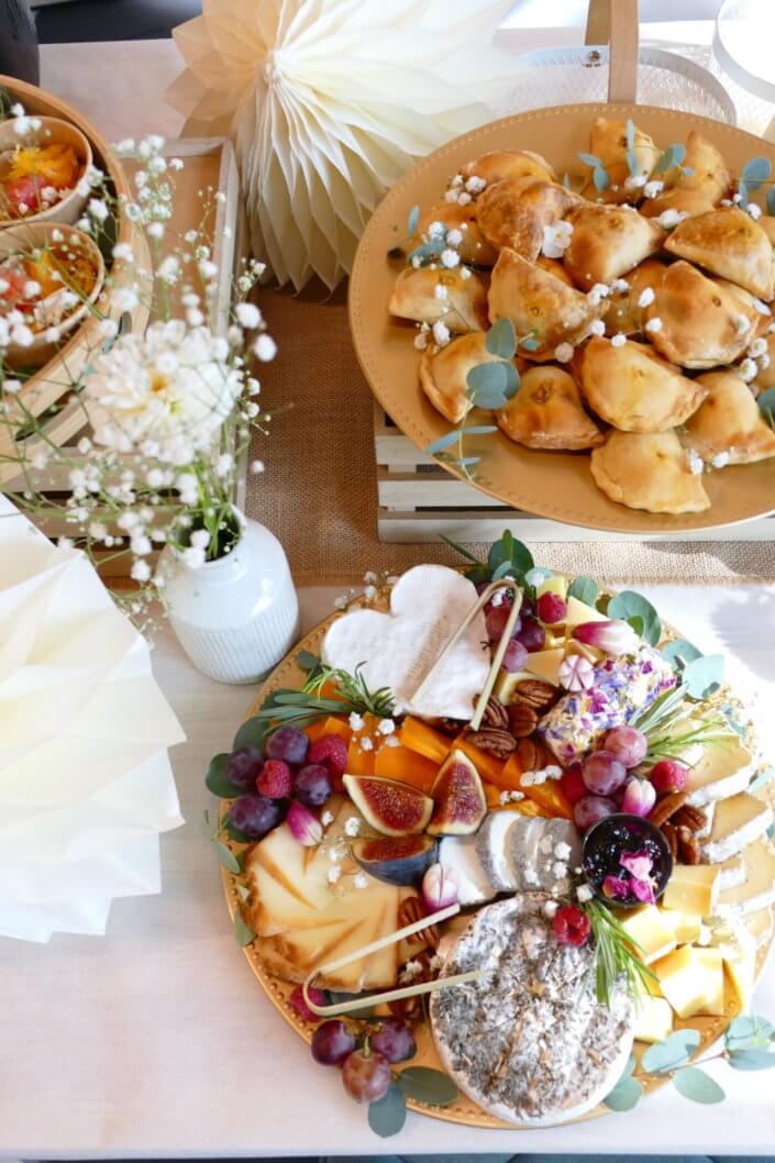 Jolie table thème mariage avec petites brochettes, salades, planche de fromages, feuilletés, sablés décorés wedding day, financiers, décoration or, blanc et petits bouquets de gypsophille