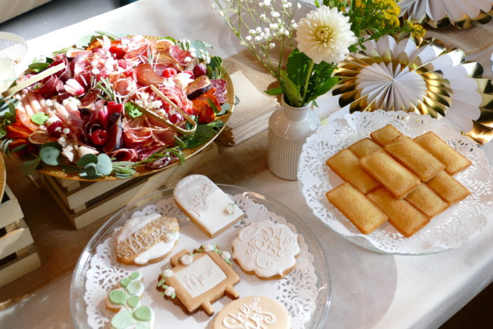 Jolie table thème mariage avec petites brochettes, salades, planche de fromages, feuilletés, sablés décorés wedding day, financiers, décoration or, blanc et petits bouquets de gypsophille