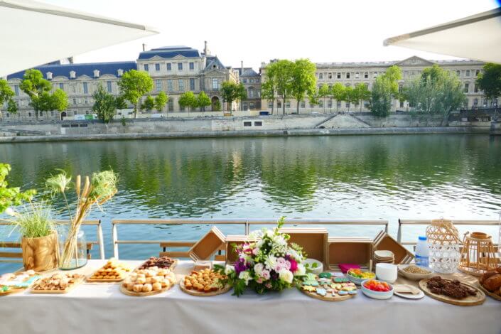 Petit déjeuner sur une péniche face au Louvre par studio Candy : beignets, financiers, sablés décorés, granola, fruits frais et décoration estivale