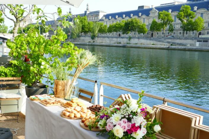 Petit déjeuner sur une péniche face au Louvre par studio Candy : beignets, financiers, sablés décorés, granola, fruits frais et décoration estivale