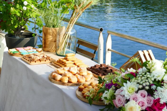 Petit déjeuner sur une péniche face au Louvre par studio Candy : beignets, financiers, sablés décorés, granola, fruits frais et décoration estivale