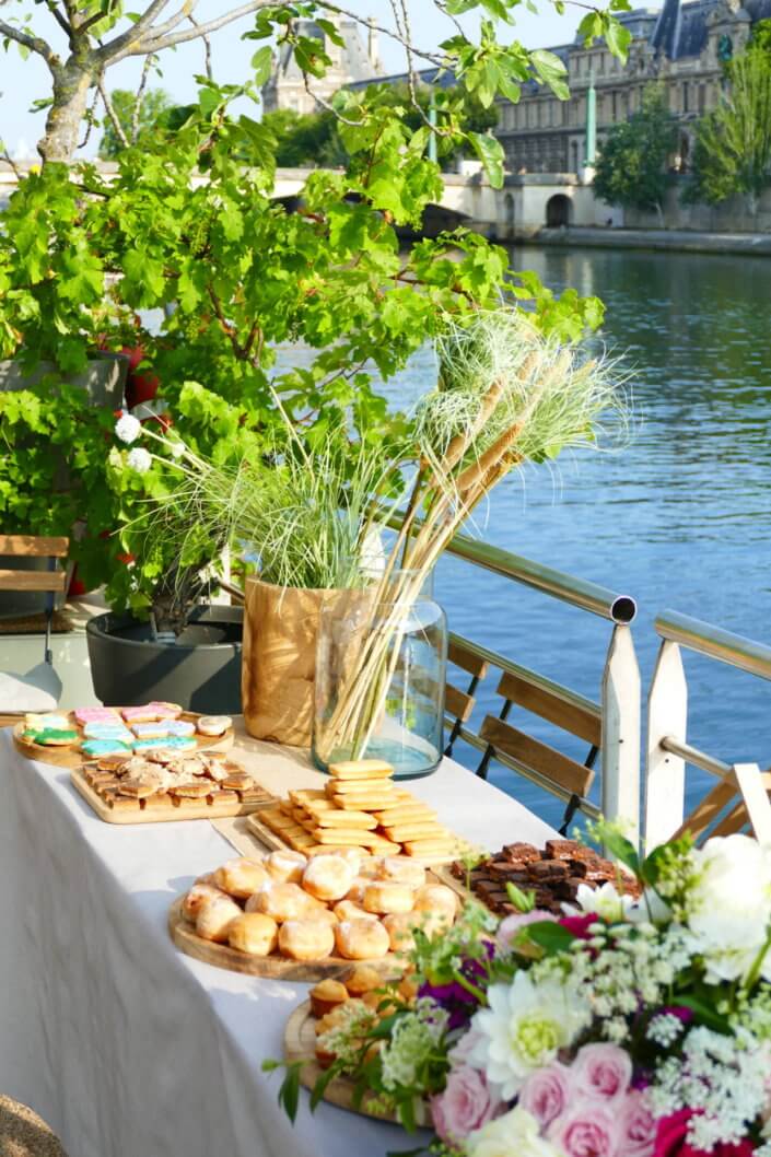 Petit déjeuner sur une péniche face au Louvre par studio Candy : beignets, financiers, sablés décorés, granola, fruits frais et décoration estivale