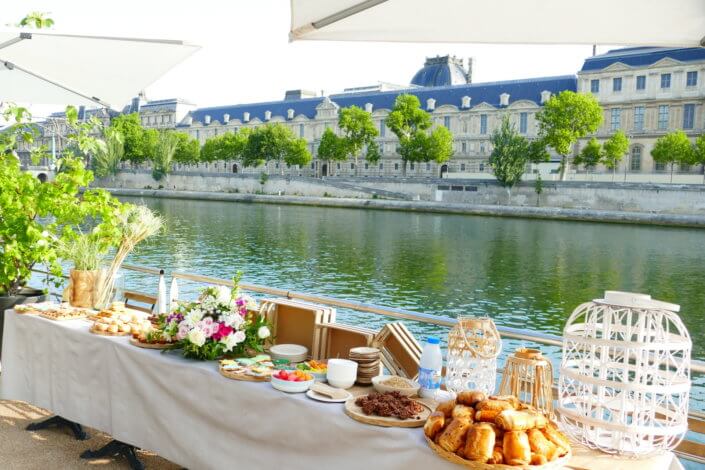 Petit déjeuner sur une péniche face au Louvre par studio Candy : beignets, financiers, sablés décorés, granola, fruits frais et décoration estivale