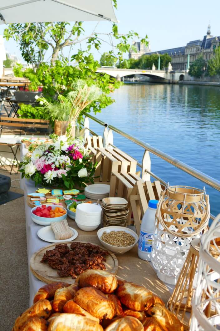 Petit déjeuner sur une péniche face au Louvre par studio Candy : beignets, financiers, sablés décorés, granola, fruits frais et décoration estivale