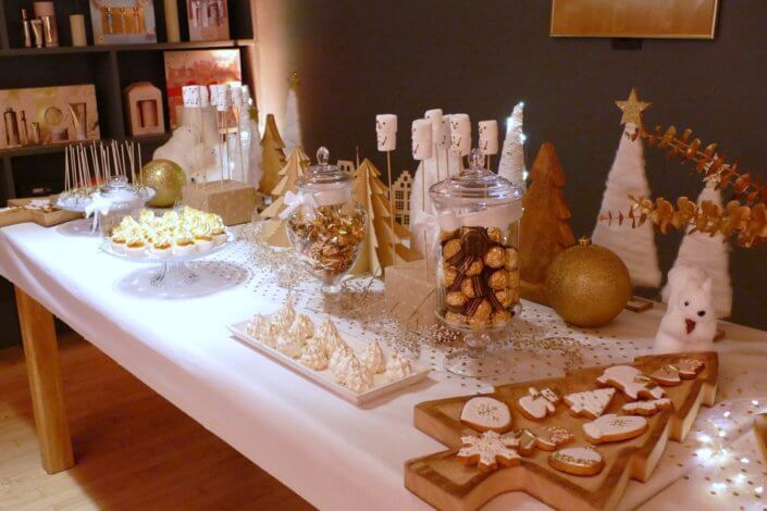 Soirée de Noël Adopt par Studio Candy avec une grande table de Noël décorée en or et blanc. Cakepops au chocolat, cupcakes, sapins meringue, sablés de Noël et corbeille de fruits et cocktail salé avec verrines, grazing platters, cônes garnis